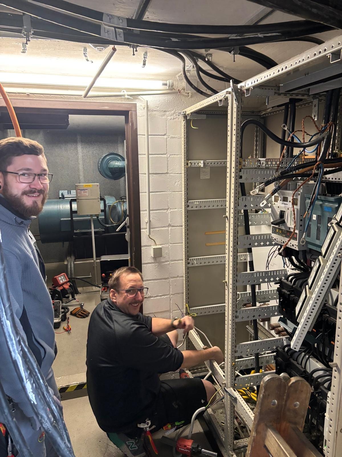 Zwei Monteure von Elektro Andres bei der Arbeit an einer offenen Verteilung im Technikraum